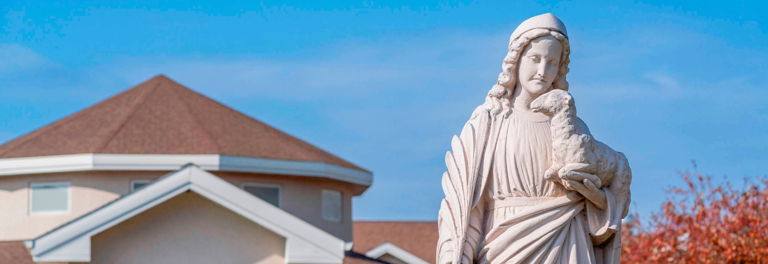 Image: a statue of St. Agnes outside the CSA motherhouse on a sunny day