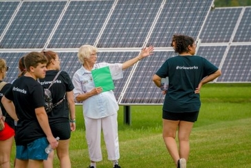 Sister Josephine stands in front of a solar panel with a small group and points ahead.